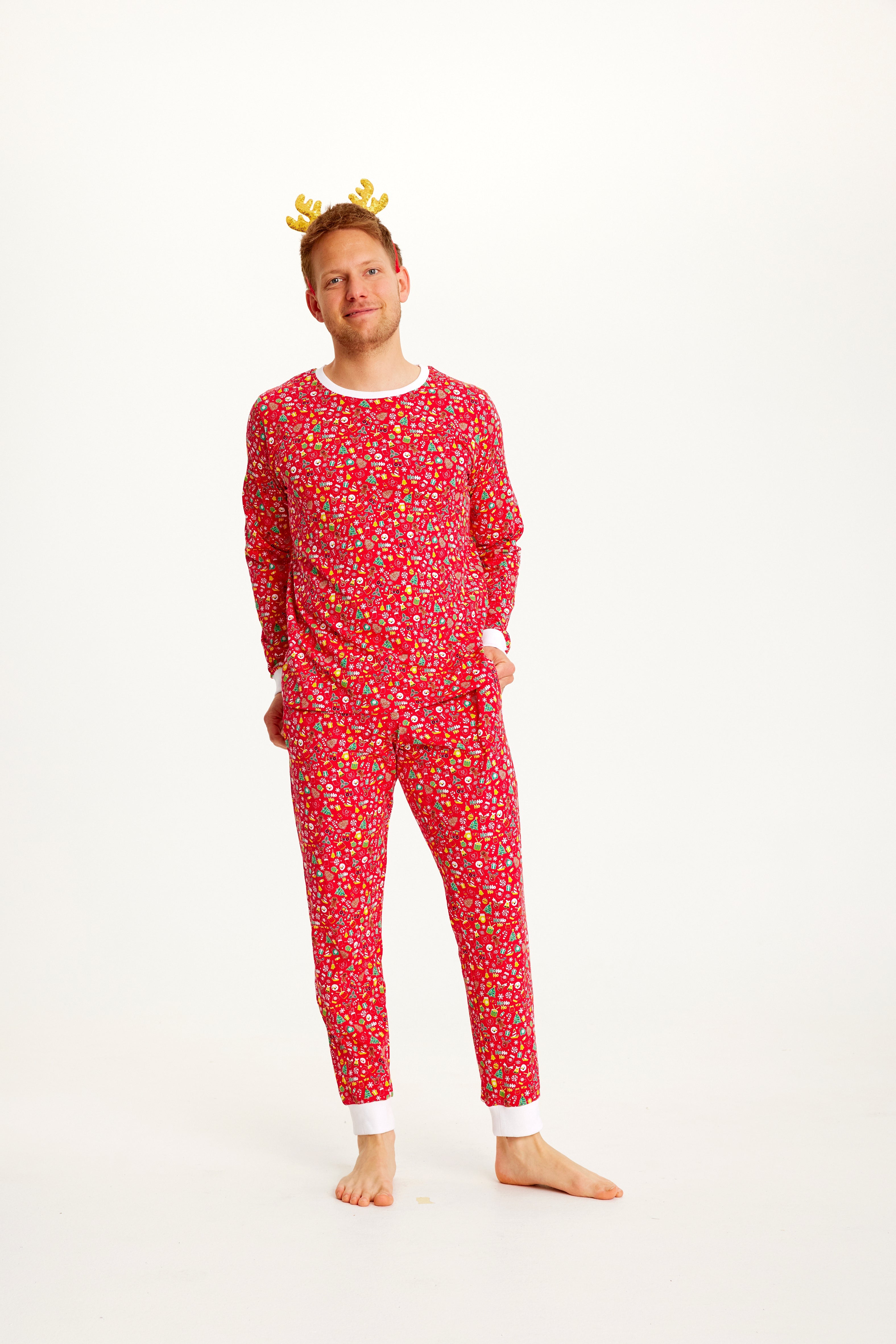 En mand står og poserer i en postkasserød pyjamas med julemønster.